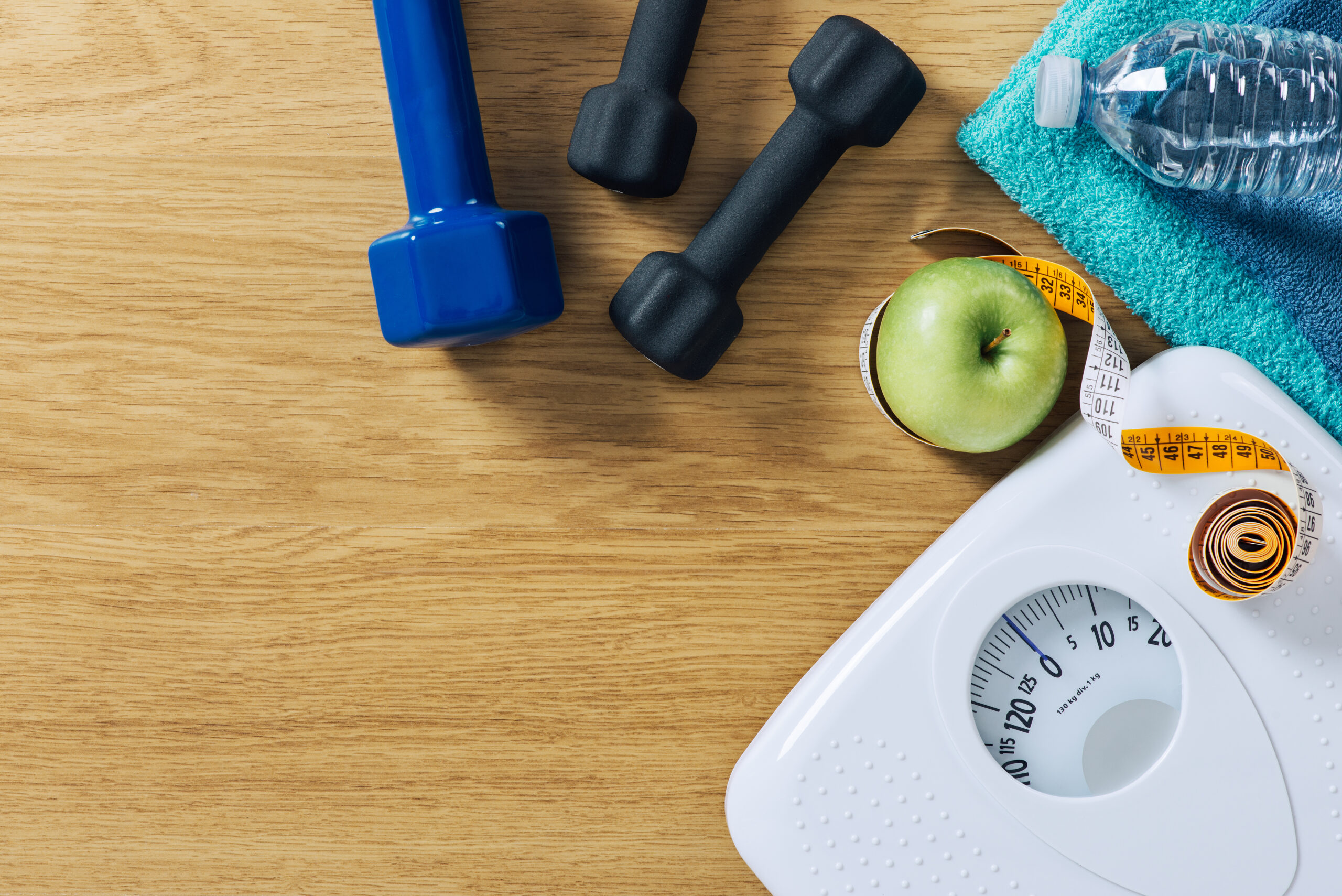 Fitness and weight loss concept, dumbbells, tape measure, white scale towels and water bottle on a wooden table, top view